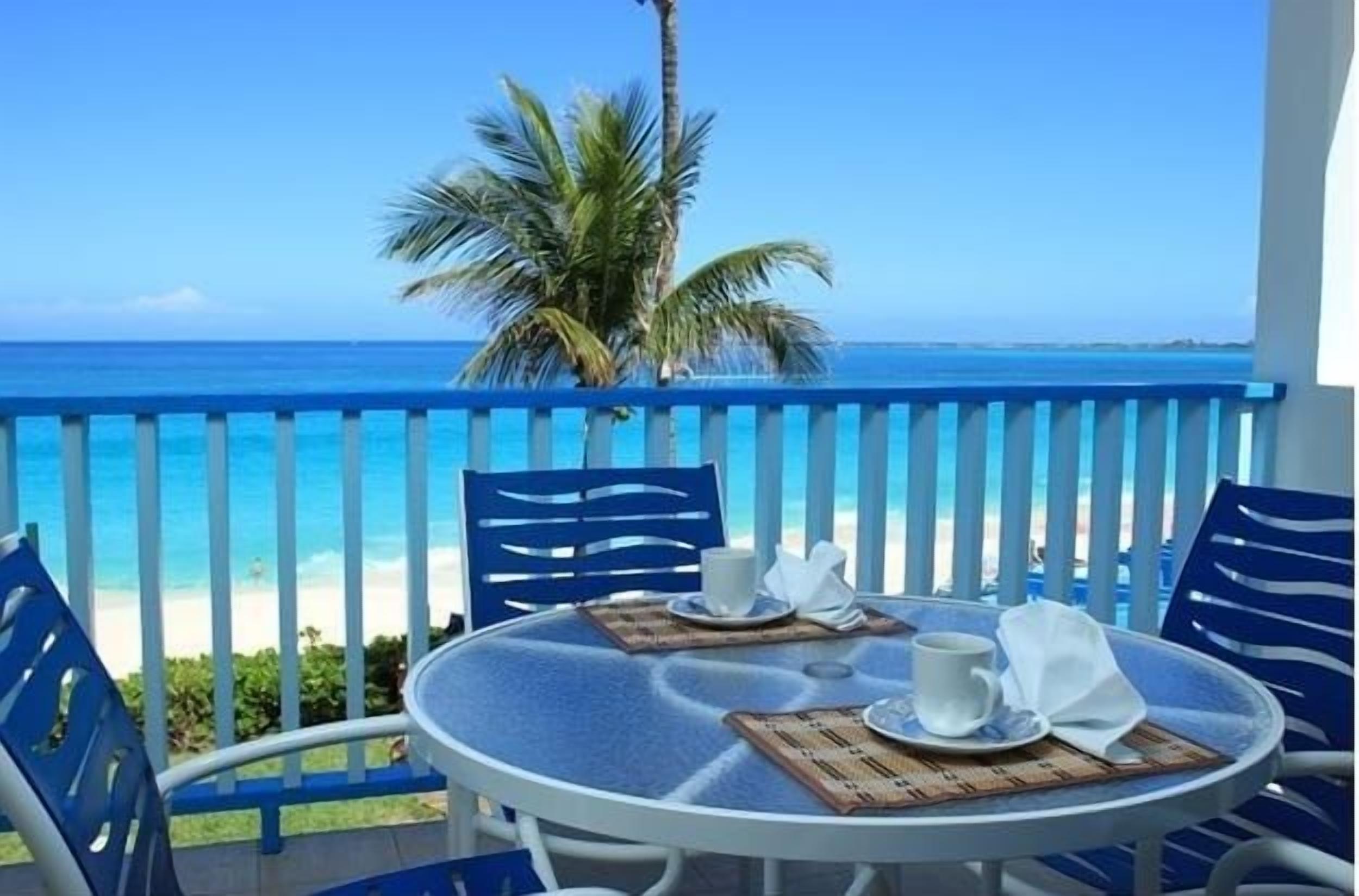 Une table ronde entourée de chaises, sur un balcon donnant sur une plage.