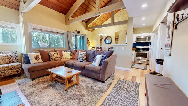 A cozy living room with a sectional sofa, a coffee table, and a kitchen area with a microwave and oven.