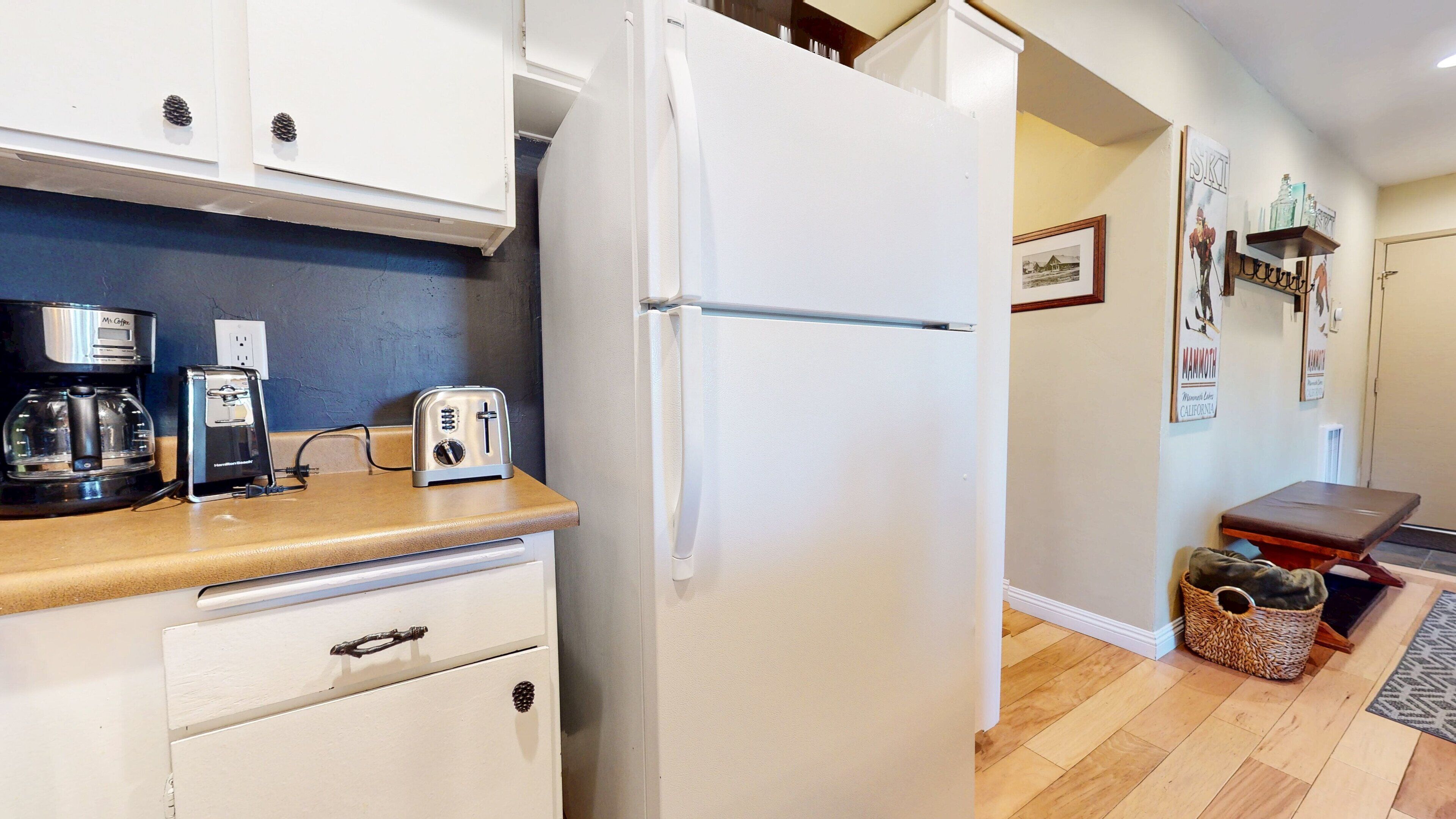 Una cocina compacta con refrigerador, cafetera, tostadora y una pequeña mesa.
