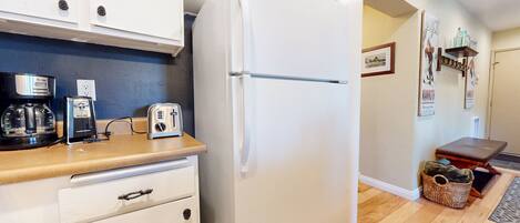 Una cocina compacta con refrigerador, cafetera, tostadora y una pequeña mesa.