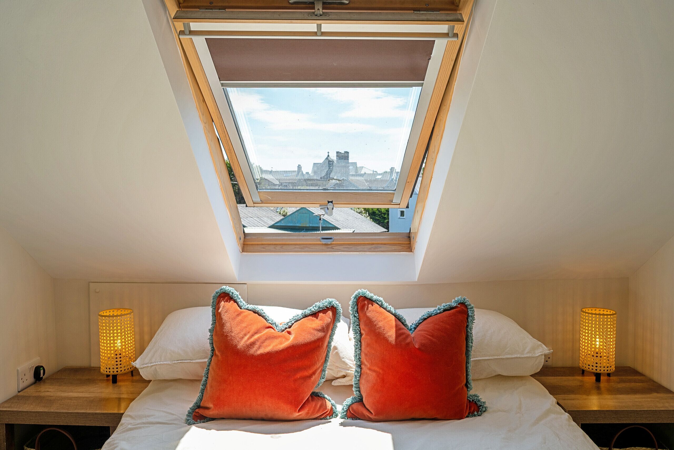 A bedroom with a skylight, two red pillows, a white bedspread, and two wall-mounted lamps.