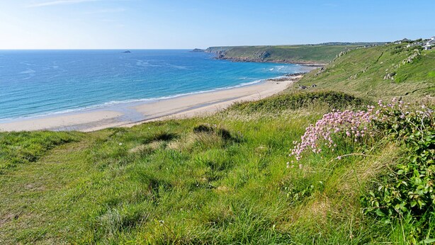 A coastal landscape with a beach, grassy hills, and a clear sky.