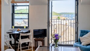 A room with a dining area, a TV, a balcony with a view of boats and hills.