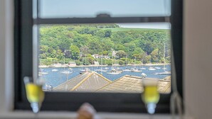 A view of a harbor with boats, a green hillside, and a window with two glasses of wine.