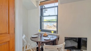 A dining area with a table, chairs, a TV, and a window with a view of a body of water and buildings.