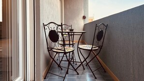 Ein kleiner Balkon mit Tisch und Stühlen, einem Fenster und einer strukturierten Wand.