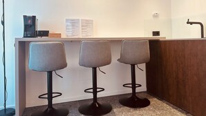 Eine moderne Bar mit drei grauen Barhocker, einer Kaffeemaschine und einer Speisekarte.