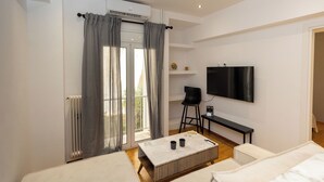 A modern hotel room with a large window, a flat-screen TV, a small table, and a sofa. - Nova Domo (Athens)