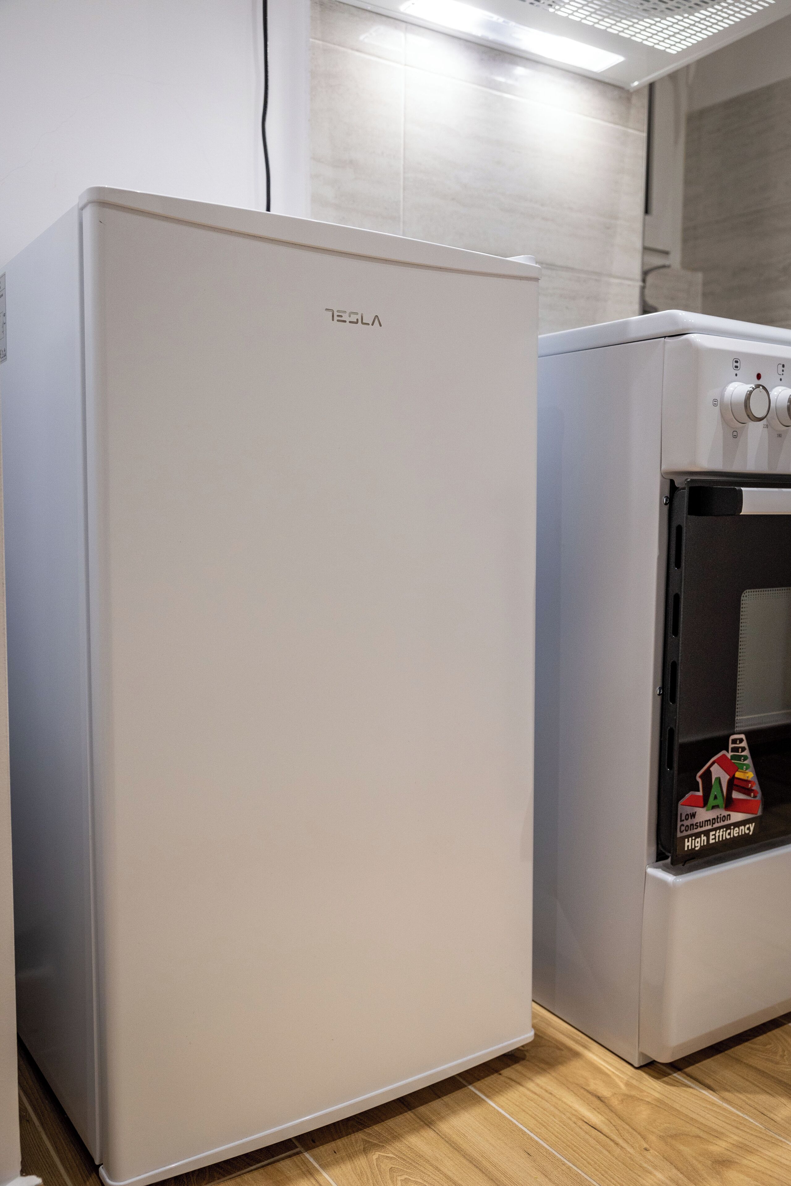 Un refrigerador y horno Tesla blancos en una cocina con piso de madera.