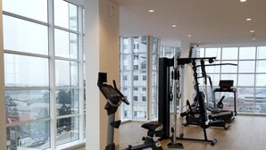 Una palestra con attrezzature per esercizi, ampie finestre e vista sulla città.