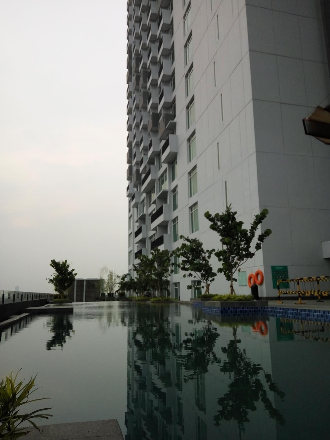 Un immeuble moderne de grande hauteur, avec une piscine dont la surface réfléchit la lumière, situé devant le bâtiment.
