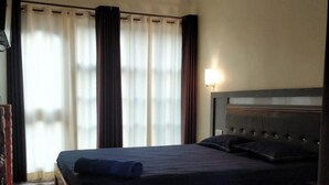 Une chambre à coucher avec un lit en bois, un ventilateur de plafond, une fenêtre avec des rideaux et une table de chevet avec une lampe.