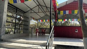 Un espace extérieur abrité, accessible par des marches menant à une plateforme, le tout entouré d’un mur rouge et d’une rambarde en métal.