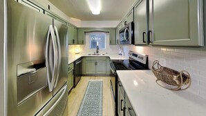 A modern kitchen with stainless steel appliances, light green cabinets, and a white countertop. - Whispering Pines 512 | Modern + Resort Amenities (Pigeon Forge)