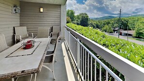 A balcony with a table and chairs, a railing, and a view of greenery and a road. - Whispering Pines 512 | Modern + Resort Amenities (Pigeon Forge)