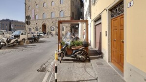 A narrow street with parked scooters and cars, a building with a stone facade, and a yellow building with a wooden door. - Green Dragon - Bright apartment with Arno view (Firenze)