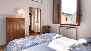 A bedroom with a bed, a wooden wardrobe, a radiator, and a window with a view of buildings. - Green Dragon - Bright apartment with Arno view (Firenze)