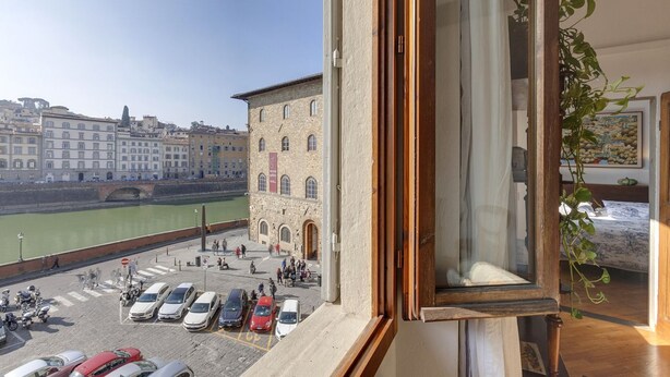 A view from a window overlooking a river with parked cars and a building with arched windows. - Green Dragon - Bright apartment with Arno view (Firenze)