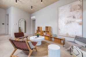 Ein modernes Wohnzimmer mit einem runden Couchtisch, zwei Ledersesseln, einem Bücherregal und einem großen abstrakten Gemälde.