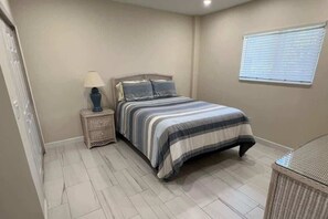 Une chambre à coucher avec un lit, une table de chevet, une lampe et une fenêtre.