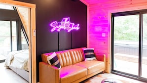 A cozy room with a leather sofa, a neon sign reading "The Sugar Shack," and a large window offering a view of the outdoors.