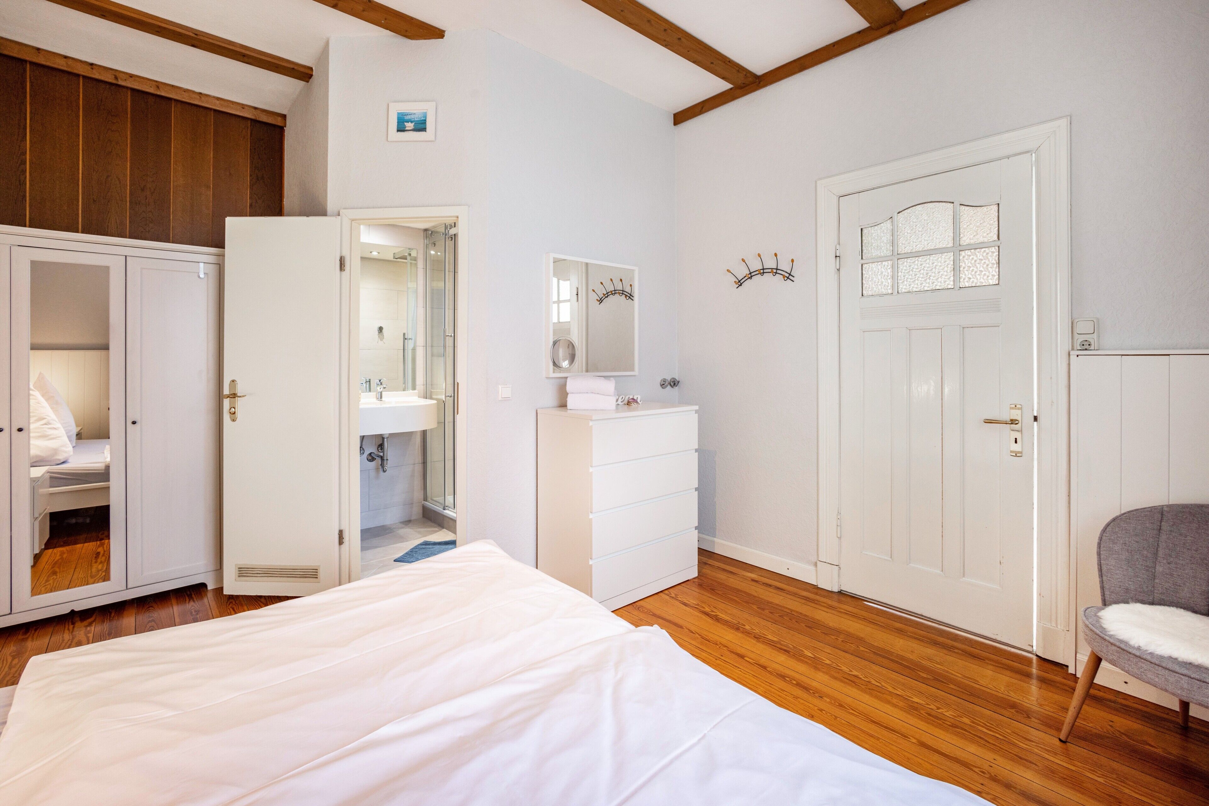 Een slaapkamer met een bed, een kledingkast, een spiegel, een deur en een stoel.