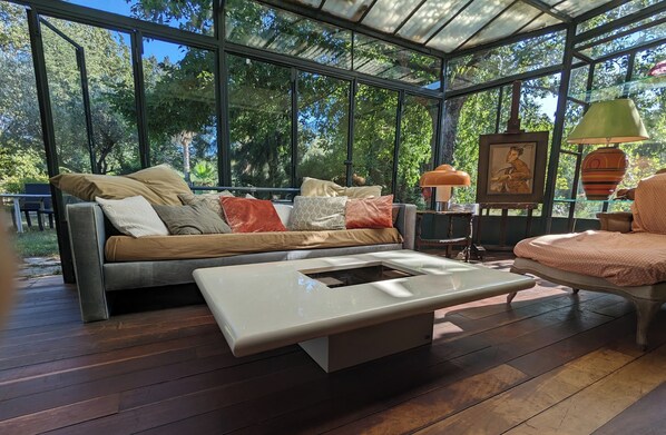 A conservatory with a wooden floor, a sofa with cushions, a table, and a lamp.