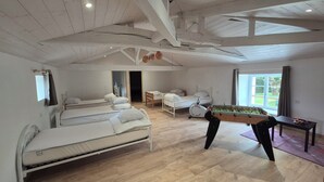 A spacious room with wooden flooring, a bed, a futon, a foosball table, and a window with a view of greenery. - Gite O Pré'Vert, Gîte Ô Pré'Vert. Group gite, tourist rental in Le Poiré Sur Vie in the Vendée. G... (Le Poiré-sur-Vie)