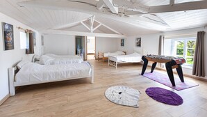 A spacious room with a high ceiling, wooden beams, a bed, a futon, a foosball table, and a window with a view. - Gite O Pré'Vert, Gîte Ô Pré'Vert. Group gite, tourist rental in Le Poiré Sur Vie in the Vendée. G... (Le Poiré-sur-Vie)