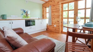 Et hyggeligt værelse i sommerhusstil med træpaneler, et tekøkken, et spiseområde med bord og stole samt en lædersofa.