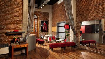 Una habitación acogedora con paredes de ladrillo, suelo de madera y muebles rojos. Hay un televisor, una mesa con una planta y un cartel en la pared.