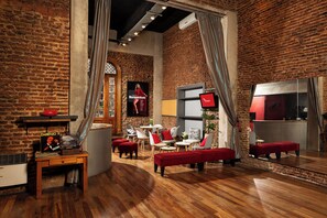 A cozy room with brick walls, a wooden floor, and red furniture. There is a TV, a table with a plant, and a poster on the wall. - Mariposita de San Telmo Hotel Boutique (Buenos Aires)