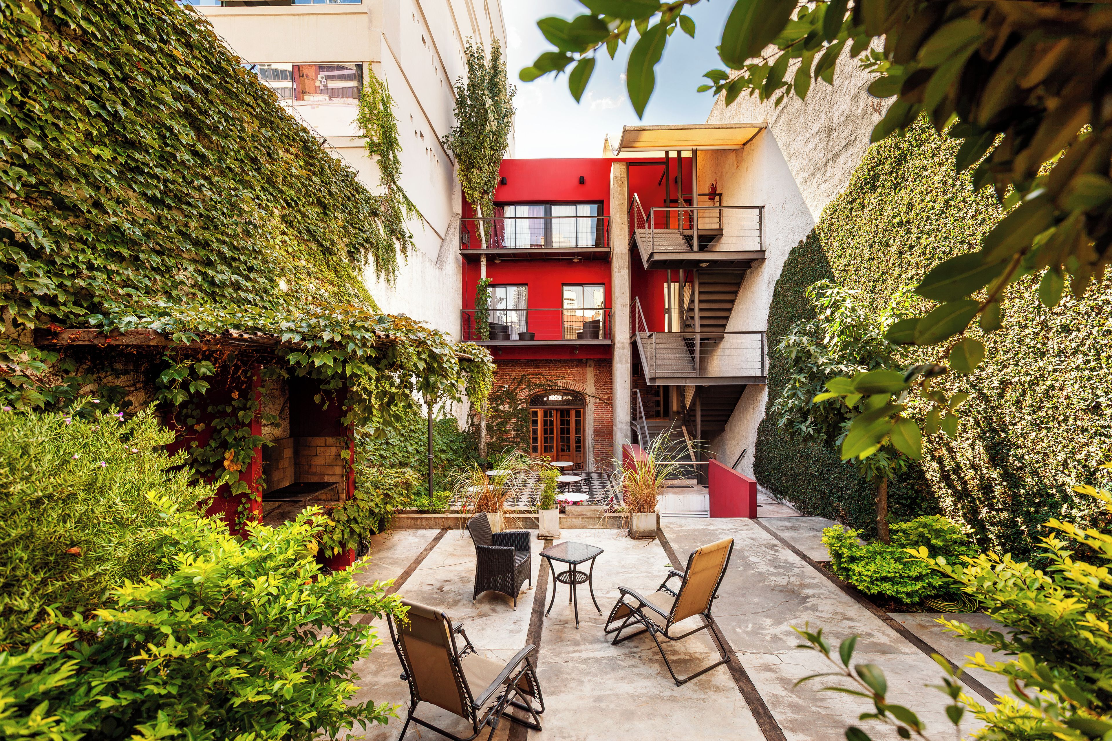 Un patio con una chimenea de ladrillo, mobiliario exterior y un edificio rojo con una escalera de incendios.