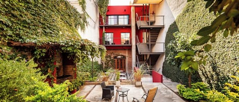 A courtyard with a brick fireplace, outdoor seating, and a red building with a fire escape.