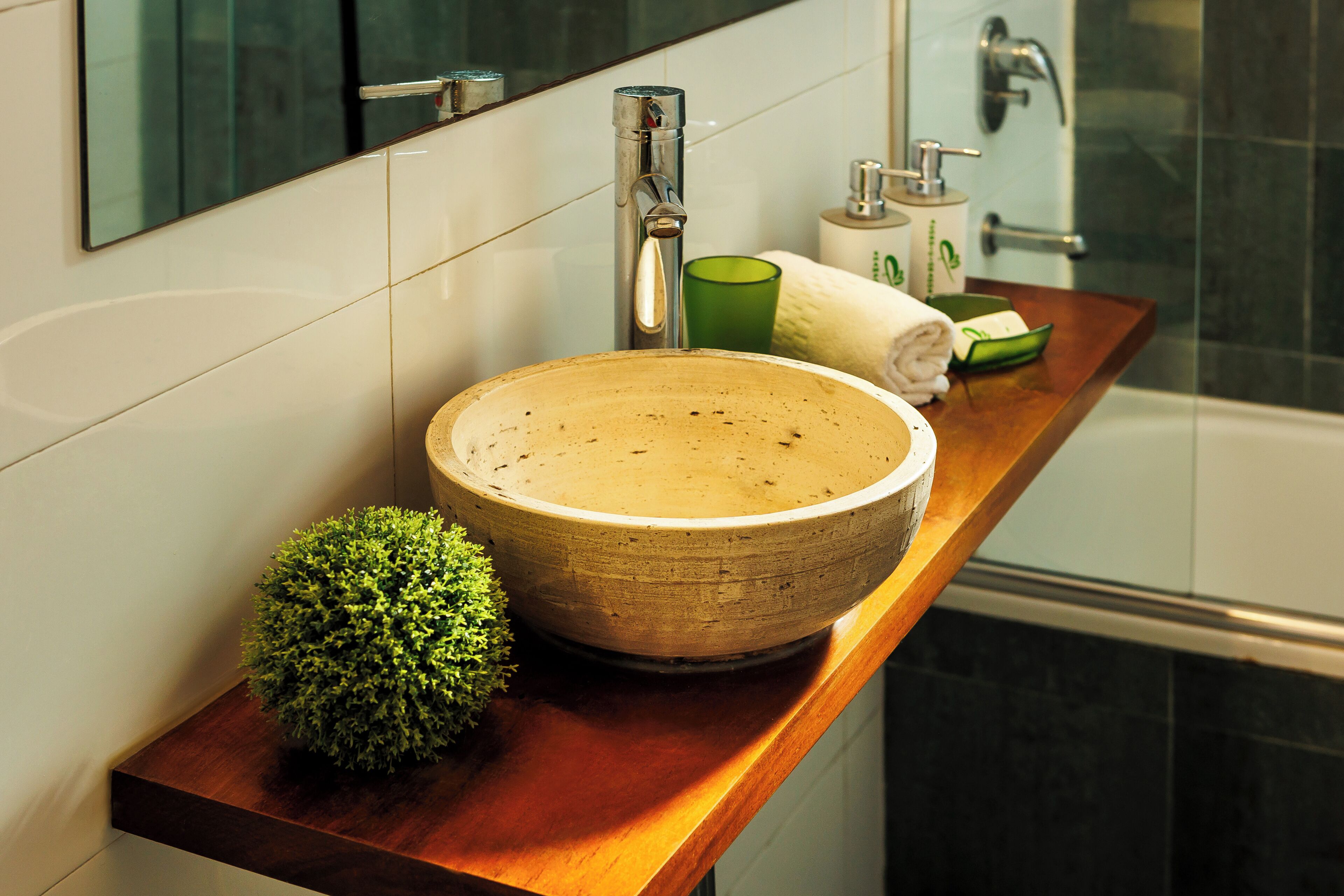 Un baño con un lavabo de cerámica redondo, un vaso de vidrio verde y una pequeña planta en maceta.