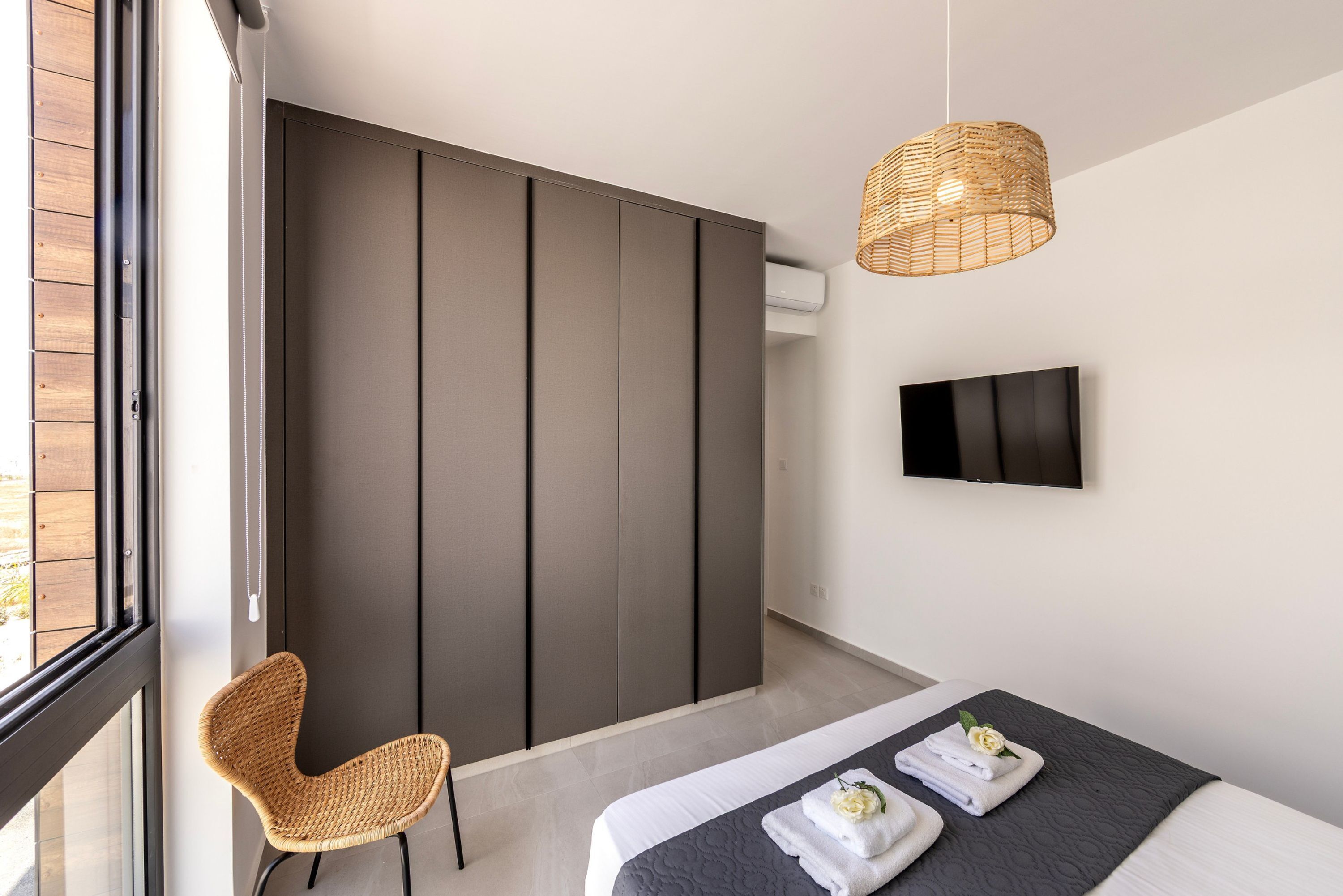 Ein modernes Schlafzimmer mit einem großen Bett, einem Korbstuhl, einer Schiebetür und einem an der Wand befestigten Fernseher.