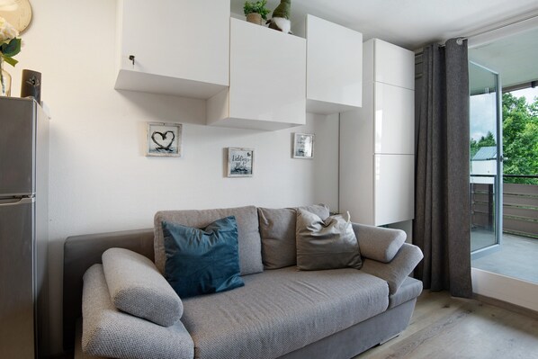 Un salón moderno con un sofá gris, armarios blancos y un ventanal con vistas a zonas verdes.
