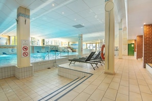 Ein Hallenbad mit gefliestem Boden, Liegestühlen und Sicherheitsschildern.