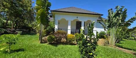 A white house with a tiled roof, surrounded by lush greenery and banana plants.