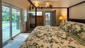 A bedroom with a four-poster bed, a sliding glass door leading to a balcony, and a view of a garden.