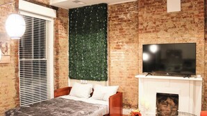 A bedroom with a bed, a brick wall, a fireplace, and a TV.