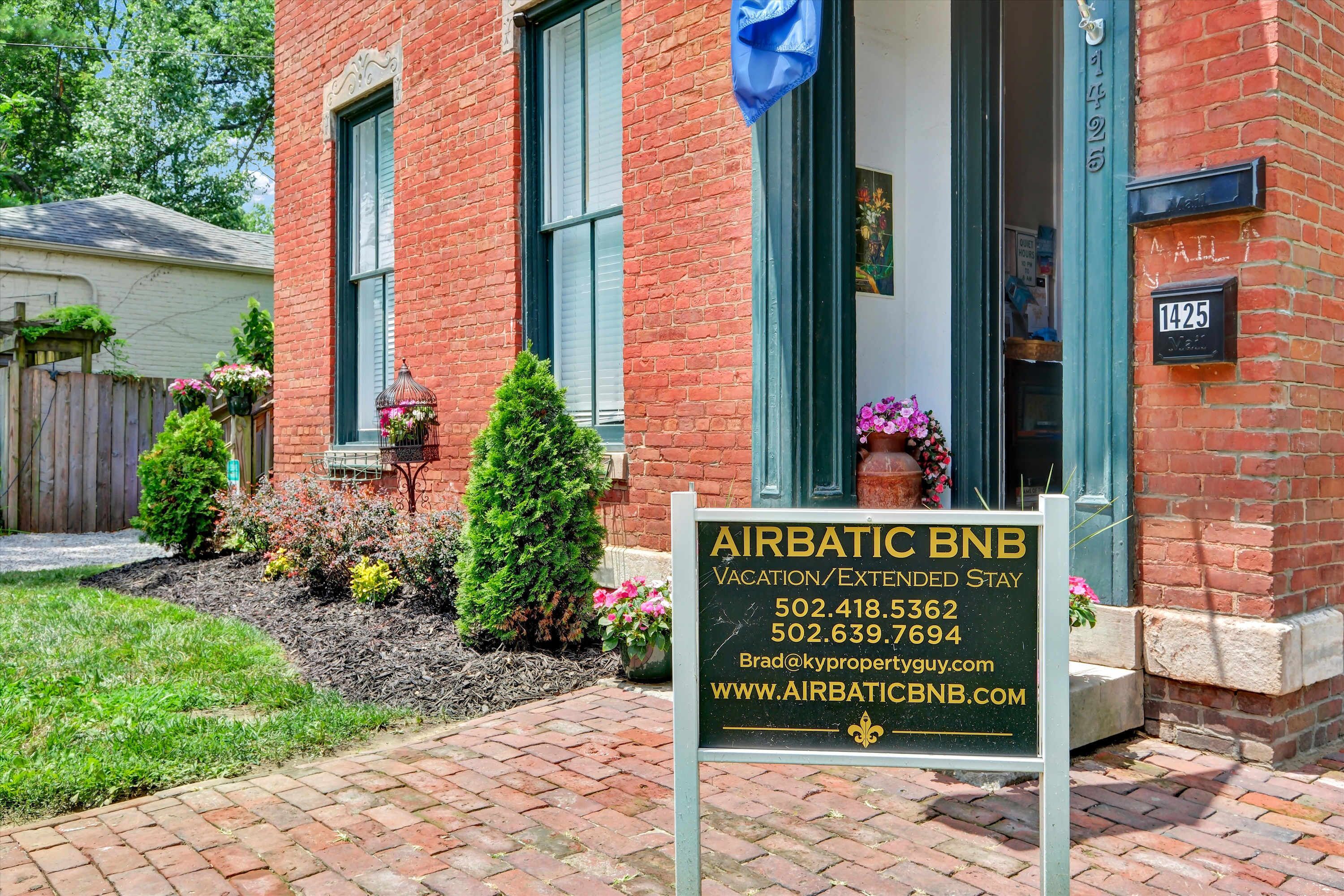 A brick building with a sign for Airbatic BNB, listing vacation and extended stay options, contact numbers, and an email address.