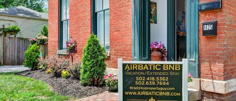 A brick building with a sign for Airbatic BNB, listing vacation and extended stay options, contact numbers, and an email address.