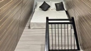 A narrow room with wooden panel walls, a bed with white bedding and black pillows, and a small window with curtains. - Serene Cabin Getaway in San Fernando City (Bacolor)