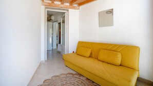 Un canapé jaune dans une pièce dont le plafond est en bois et un des murs est blanc.