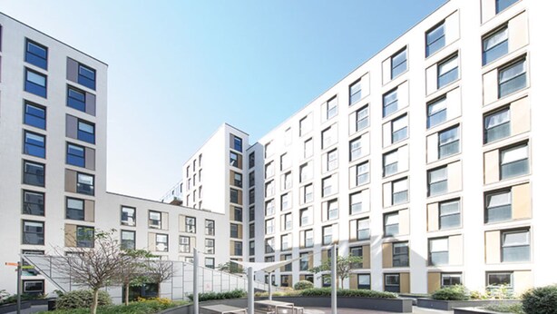 Een modern appartementencomplex met meerdere verdiepingen, balkons en een binnentuin met zitgedeeltes.