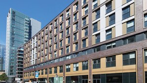 Een meerlaags hotel met een modern ontwerp, met een combinatie van baksteen en glazen gevels, grote ramen en een parkeerplaats ervoor.