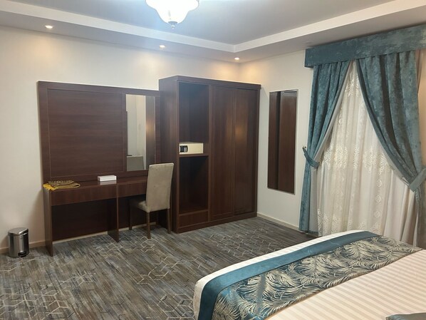 Habitación de hotel con cama, escritorio con silla, armario y un espejo grande.