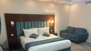 A modern hotel room with a large bed, a sofa, and a nightstand with a lamp. - Alfursan Almotahida Serviced Apartments Alhamadania Dist Baydon Street (Jeddah)