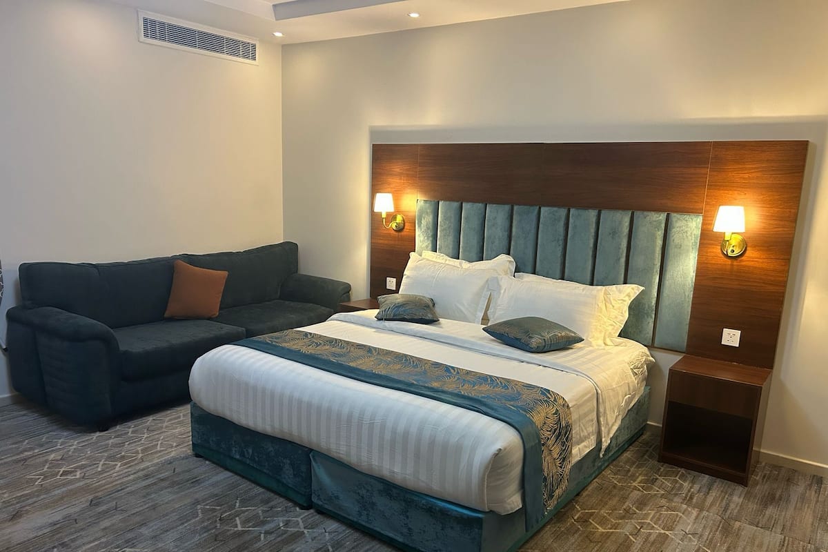 A modern hotel room with a large bed, a dark sofa, and two bedside tables with lamps.